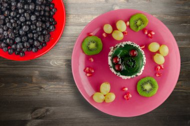 Kek ve meyve üzümleri, kivi, siyah ahşap zemin üzerinde nar. Pembe tabakta meyveli tatlı.