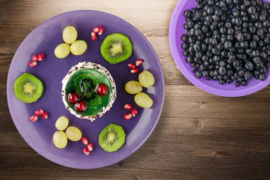 Kek ve meyve üzümleri, kivi, kahverengi ahşap zemin üzerinde nar. Mor tabak manzaralı meyveli tatlı.