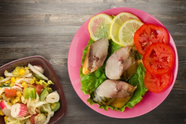 Pembe tabakta tütsülenmiş uskumru. Sebze salatanın üst manzarası. Siyah ahşap arka planda limonlu uskumru ve domates.