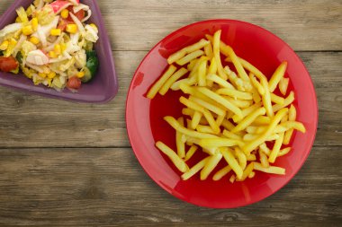 Ahşap arka planda patates kızartması. Sebze salatası manzaralı kırmızı tabakta patates kızartması.