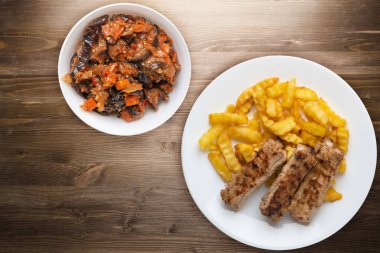 Beyaz tabakta domuz pirzolası ve patates. Kahverengi ahşap arka planda sebze salatası ve sos. Fast food 'un en iyi manzarası. Sağlıksız yiyecekler.