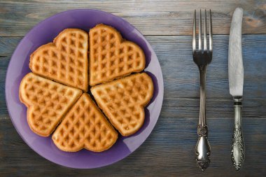 Belçika waffle 'ı mavi ahşap arka plan. Çatal ve bıçak manzaralı mor bir tabakta waffle.