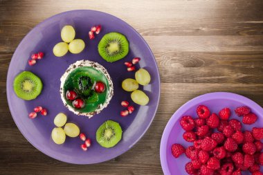 Kek ve meyve üzümleri, kivi, kahverengi ahşap zemin üzerinde nar. Mor tabak manzaralı meyveli tatlı.