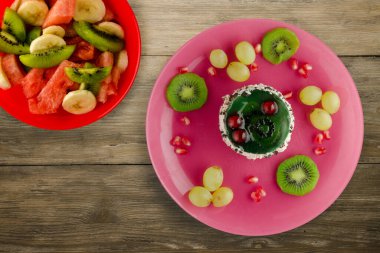 Kek ve meyve üzümleri, kivi, ahşap zemin üzerinde nar. Meyveli tatlı pembe tabak manzaralı.