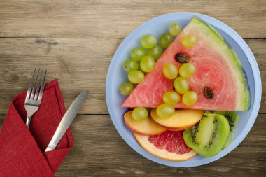 Kahverengi ahşap arka planda çatal ve bıçakla dilimlenmiş meyve. Açık mavi bir tabakta dilimlenmiş meyve manzarası