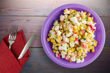 Mor tabakta çatal ve bıçak manzaralı yengeç salatası. Mor ahşap arka planda yengeç salatası