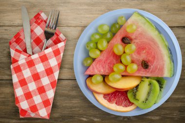 Kahverengi ahşap arka planda çatal ve bıçakla dilimlenmiş meyve. Açık mavi bir tabakta dilimlenmiş meyve manzarası