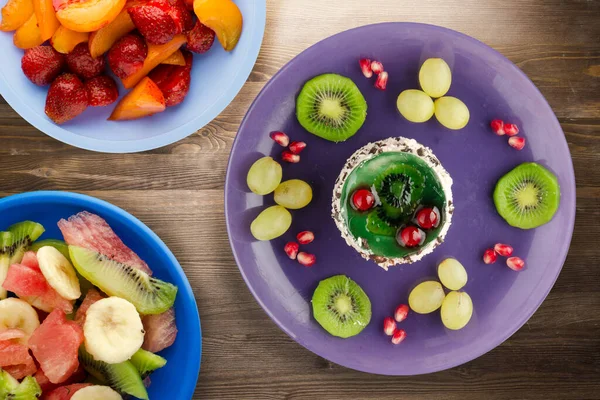 Kek ve meyve üzümleri, kivi, kahverengi ahşap zemin üzerinde nar. Mor tabak manzaralı meyveli tatlı.