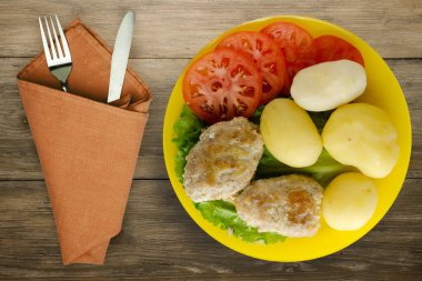 Çatal ve bıçak manzaralı sarı tabakta patatesli pirzola. Kahverengi ahşap arka planda patatesli pirzola