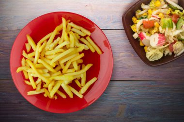 Ahşap arka planda patates kızartması. Kırmızı tabakta patates kızartması ve vejetaryen salatası.