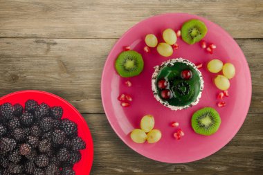 Kek ve meyve üzümleri, kivi, ahşap zemin üzerinde nar. Meyveli tatlı pembe tabak manzaralı.