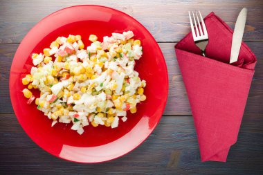 Çatal ve bıçak manzaralı kırmızı tabakta yengeç salatası. Mor ahşap arka planda yengeç salatası