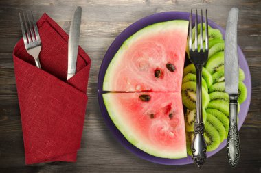 Karpuz ve kivi siyah ahşap bir zemin üzerinde mor bir tabakta dilimlendi. 