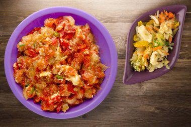 Kahverengi ahşap arka planda mor tabakta soğanlı haşlanmış domatesler. Soğan manzaralı haşlanmış domates. Sebze salatalı vejetaryen yemeği