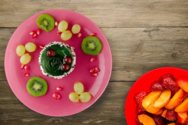 Kek ve meyve üzümleri, kivi, ahşap zemin üzerinde nar. Meyveli tatlı pembe tabak manzaralı.