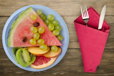 Ahşap bir arka planda dilimlenmiş meyve. Dilimlenmiş meyve, açık mavi bir tabakta üst görünümde. Dilimlenmiş meyve, çatal ve bıçak.