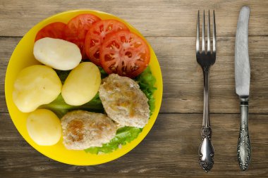 Çatal ve bıçak manzaralı sarı tabakta patatesli pirzola. Kahverengi ahşap arka planda patatesli pirzola