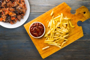 Gri mavi ahşap arka planda ketçaplı patates kızartması. Kahverengi ahşap tabakta patates kızartması ve vejetaryen salata.