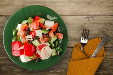 Kahverengi ahşap arka planda Yunan salatası. Çatal ve bıçak manzaralı yeşil tabakta Yunan salatası. sağlıklı yiyecekler