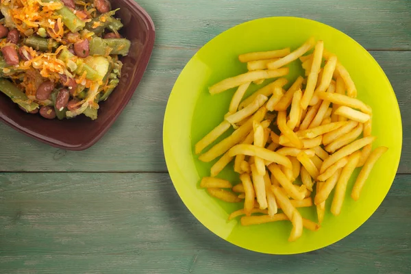 Patatesleri yeşil ahşap arka planda kızart. Limonlu patates kızartması ve sebze salatası.