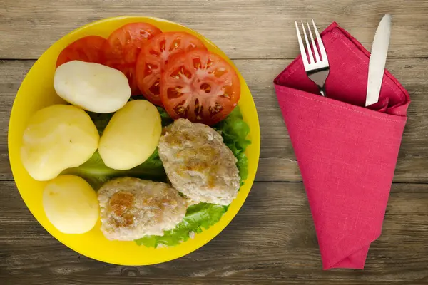 Çatal ve bıçak manzaralı sarı tabakta patatesli pirzola. Kahverengi ahşap arka planda patatesli pirzola