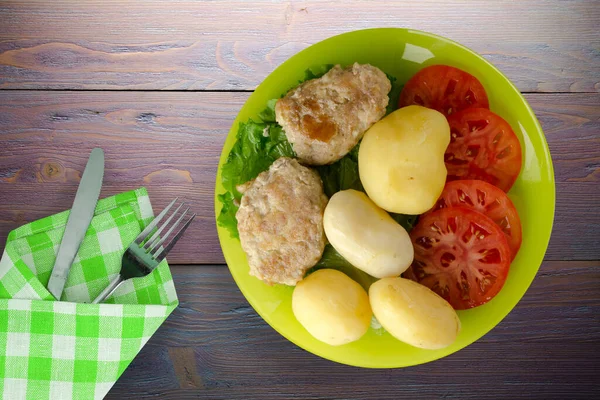 Kireç tabağında patates ve çatal ve bıçak manzaralı pirzola. Patatesli pirzola ve mor ahşap arka plan.