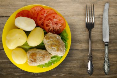 Çatal ve bıçak manzaralı sarı tabakta patatesli pirzola. Kahverengi ahşap arka planda patatesli pirzola