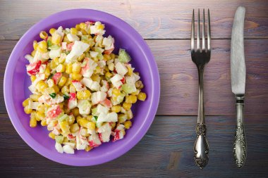 Mor tabakta çatal ve bıçak manzaralı yengeç salatası. Mor ahşap arka planda yengeç salatası