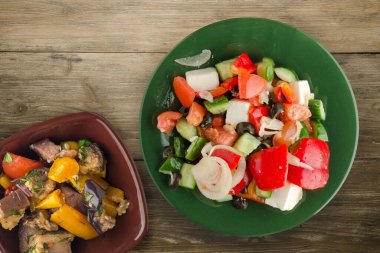 Kahverengi ahşap arka planda Yunan salatası. Vejetaryen salata manzaralı yeşil tabakta Yunan salatası. sağlıklı yiyecekler