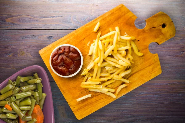 Patates kızartması ve mor ahşap arka planda ketçap. Kahverengi ahşap tabakta patates kızartması ve vejetaryen salata.