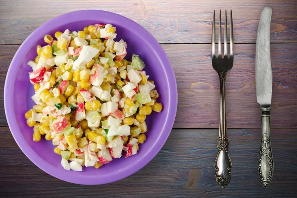 Mor tabakta çatal ve bıçak manzaralı yengeç salatası. Mor ahşap arka planda yengeç salatası