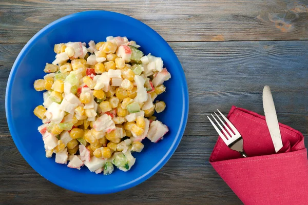 Çatal ve bıçak manzaralı lacivert tabakta yengeç salatası. Gri ve mavi ahşap arka planda yengeç salatası
