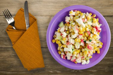 Mor tabakta çatal ve bıçak manzaralı yengeç salatası. Kahverengi ahşap arka planda yengeç salatası