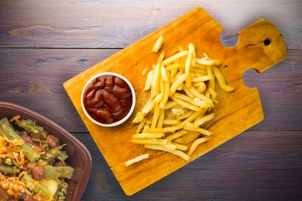 Patates kızartması ve mor ahşap arka planda ketçap. Kahverengi ahşap tabakta patates kızartması ve vejetaryen salata.