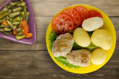 Sarı tabakta patates ve sebze salatası manzaralı pirzola. Kahverengi ahşap arka planda patatesli pirzola