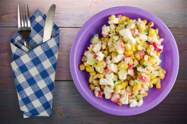 Mor tabakta çatal ve bıçak manzaralı yengeç salatası. Mor ahşap arka planda yengeç salatası