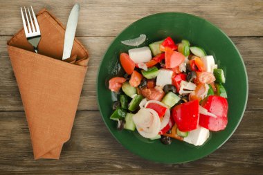 Kahverengi ahşap arka planda Yunan salatası. Çatal ve bıçak manzaralı yeşil tabakta Yunan salatası. sağlıklı yiyecekler