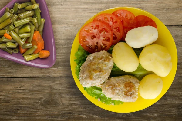 Sarı tabakta patates ve sebze salatası manzaralı pirzola. Kahverengi ahşap arka planda patatesli pirzola