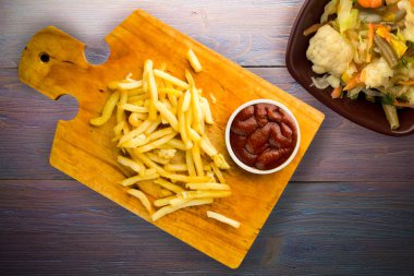 Patates kızartması ve mor ahşap arka planda ketçap. Kahverengi ahşap tabakta patates kızartması ve vejetaryen salata.