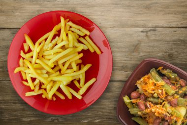 Ahşap arka planda patates kızartması. Sebze salatası manzaralı kırmızı tabakta patates kızartması.