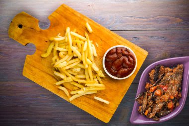 Patates kızartması ve mor ahşap arka planda ketçap. Kahverengi ahşap tabakta patates kızartması ve vejetaryen salata.