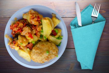 Patatesli pirzola ve fırında domates. Açık mavi tabakta pirzola çatal ve mor ahşap arka planda bıçak.