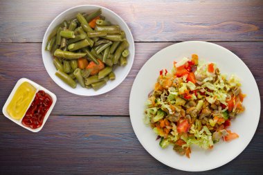 Tavuk mideli salata ile sebze havuç, soğan, biber, lahana, domates, brokoli. Mor ahşap arka planda beyaz tabakta tavuklu salata.