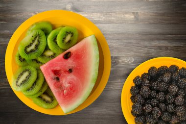 Sarı bir tabakta karpuz ve kivi dilimlenmiş ya da siyah ahşap bir arka plan.