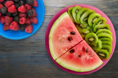 Kırmızı bir tabakta karpuz ve kivi dilimlenmiş mavi gri ahşap arka plan manzaralı meyve salatası.