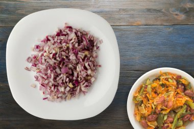 Mavi gri ahşap arka planda kırmızı soğan. Beyaz tabakta doğranmış kırmızı soğan ve vejetaryen salata.