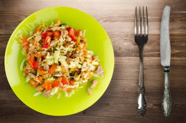 Tavuk mideli salata ile sebze havuç, soğan, biber, lahana, domates, brokoli. Kireç tabağında tavuk salatası, kahverengi ahşap arka planda çatal ve bıçak manzaralı.