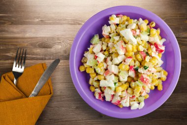 Mor tabakta çatal ve bıçak manzaralı yengeç salatası. Kahverengi ahşap arka planda yengeç salatası