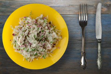salata daikon, soğan ve dereotu mavi gri ahşap arka planda. Çatal ve bıçak manzaralı sarı tabakta salata.