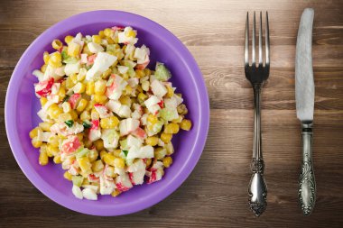 Mor tabakta çatal ve bıçak manzaralı yengeç salatası. Kahverengi ahşap arka planda yengeç salatası